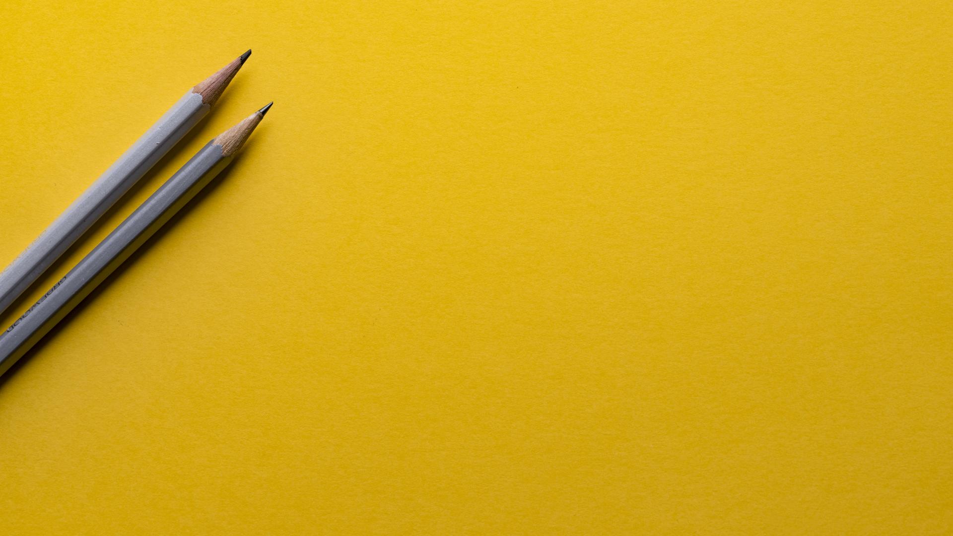 Two pencils laying on a yellow background